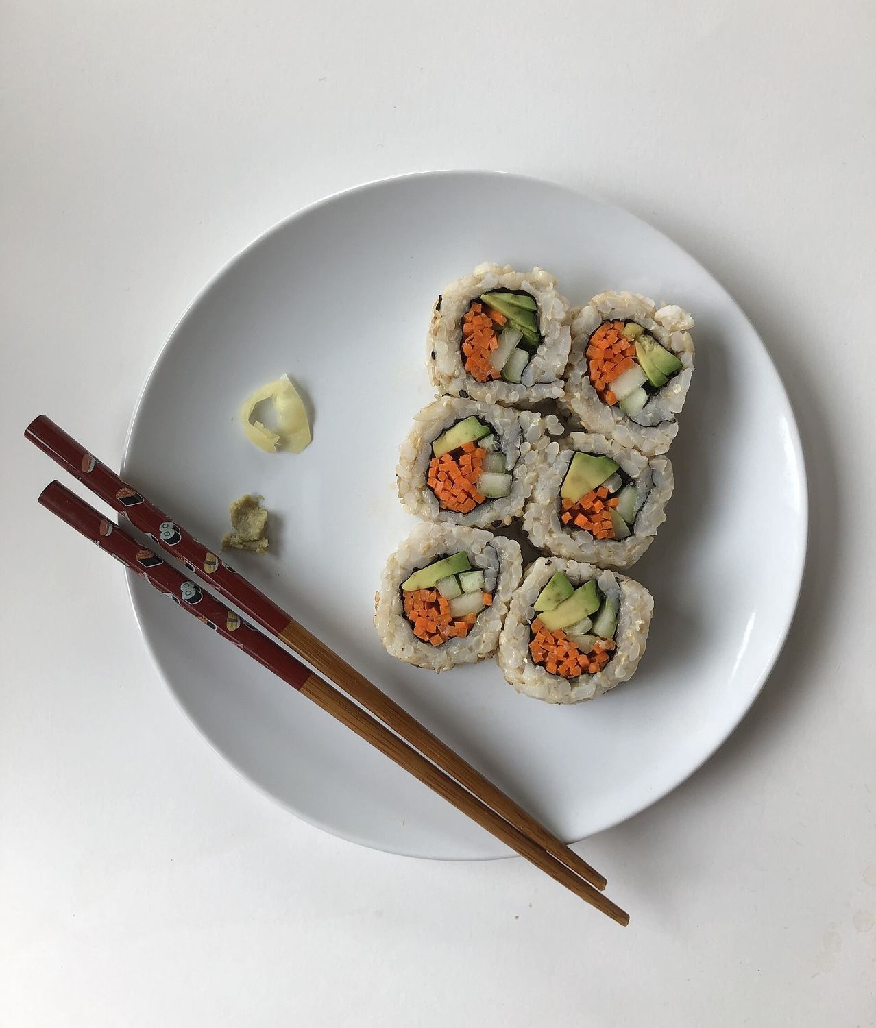 Sei pezzi di maki con riso integrale, carota, cetriolo e avocado su un piatto bianco, con le bacchette