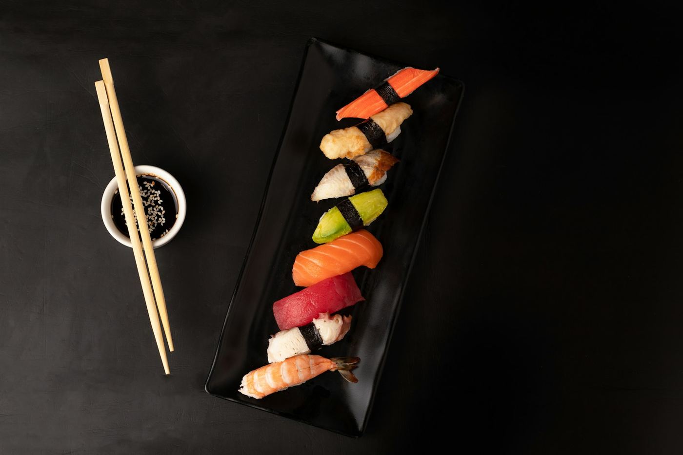 Nigiri assortiti su un piatto nero allungato, con bacchette e salsa di soia