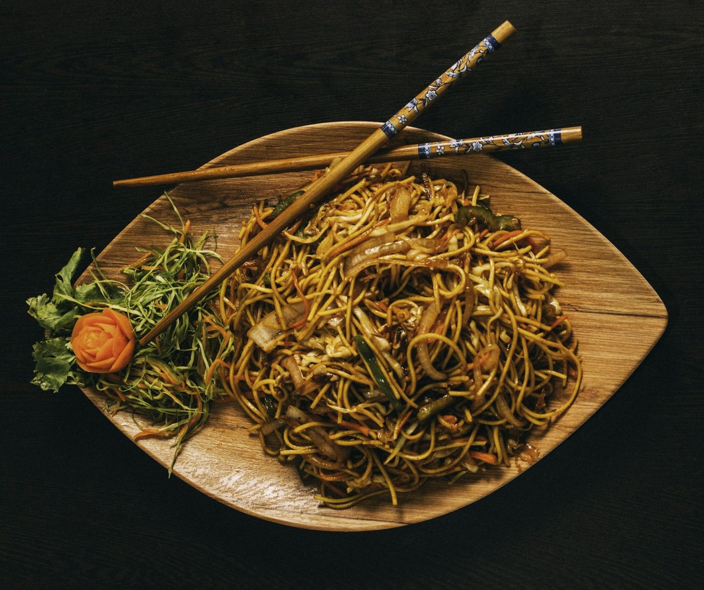 Spaghetti saltati con verdure su un piatto di legno, con le bacchette